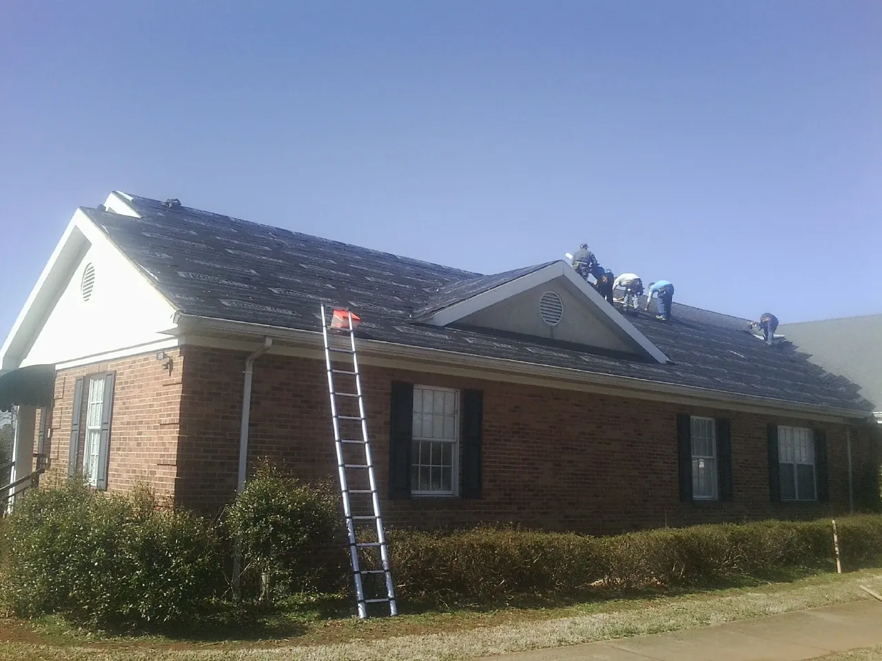 Crew tearing shingles off a brick ranch roof with a ladder set — Emergency Roof Repair work by our crew in Lookeba