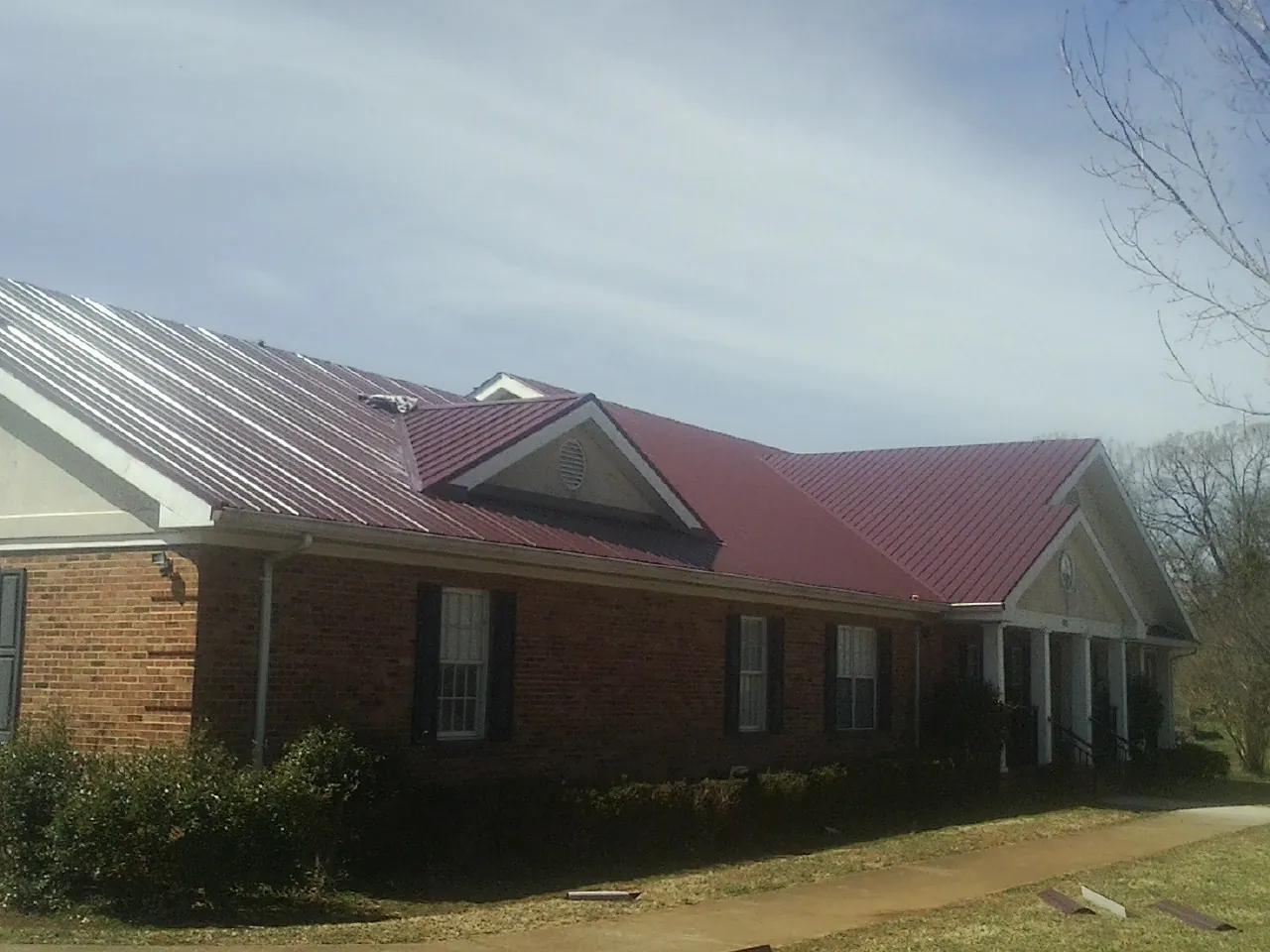 Red metal roof with gabled entries on a long brick building, from a Hail Damage Roof Repair job in Lookeba