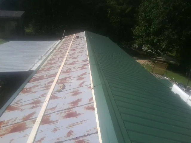 Old rusted panels beside newly installed green metal roofing — Wind Damage Roof Repair by Roofing Brothers in Lookeba