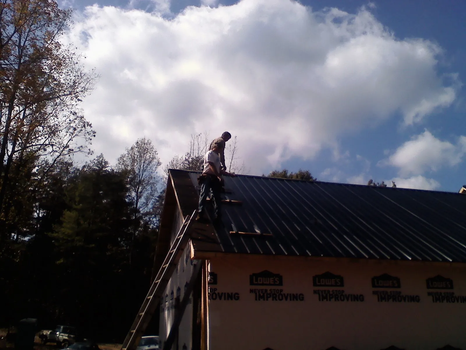 Roofer fastening dark metal panels high against a cloudy sky, from a Roof Inspection job in Lookeba
