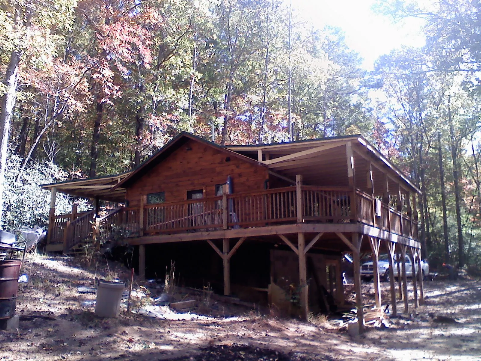 Log cabin with a wraparound porch and metal roof in the fall in Lookeba