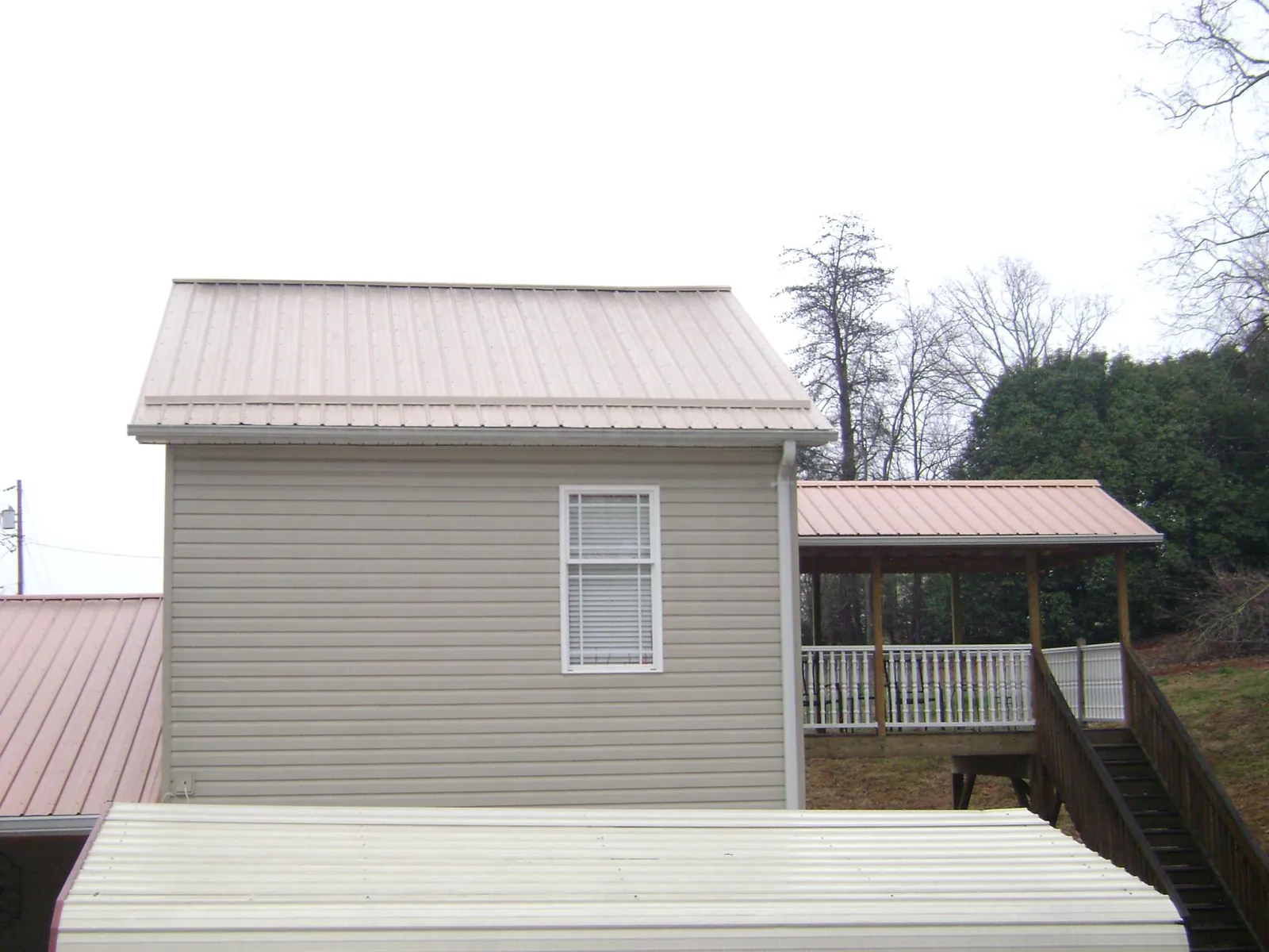Tan metal roofs on a two story addition and attached porch, from a Roof Replacement job in Lookeba